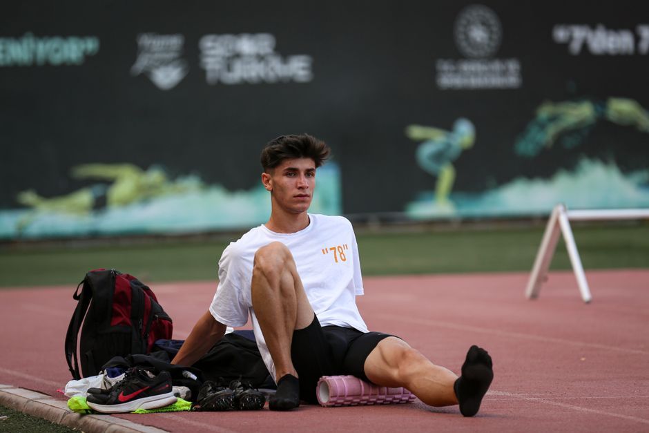 Athlete in sportswear using a foam roller on a track, preparing for training.