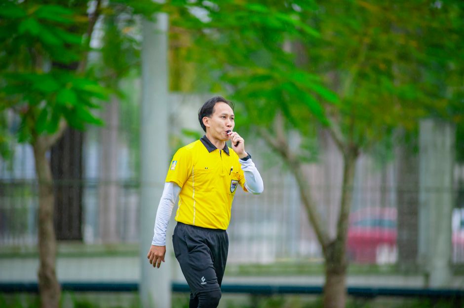 A referee in a yellow shirt blows a whistle during a soccer match in Hanoi, Vietnam.